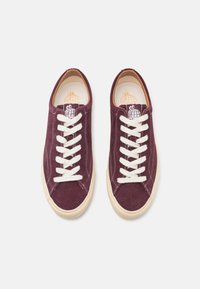 Burgundy suede sneakers with white laces, rounded toe, and cream rubber sole. Features a logo on the insole. Flat, smooth texture.