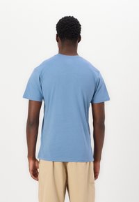 Kortærmet, rundhalset t-shirt i lyseblåt bomuldsstof, med et enkelt design uden synlige mønstre eller detaljer, set fra ryggen.