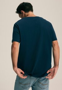 Granatowa bawełniana koszulka z krótkim rękawem i okrągłym dekoltem, o luźnym kroju i gładkiej fakturze, noszona z jasnoniebieskimi dżinsami.