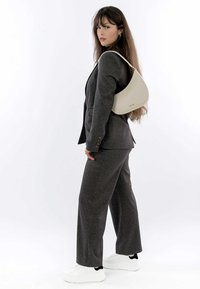 Grau maßgeschneiderter Anzug mit weit geschnittenen Hosen, kombiniert mit weißen Sneakers. Eine cremefarbene Tasche hängt über der Schulter. Einfaches und modernes Design.