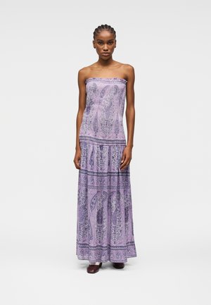 Donna che indossa un abito viola senza spalline, lungo fino al pavimento, con motivo paisley, in piedi con le braccia rilassate lungo i fianchi su uno sfondo semplice.
