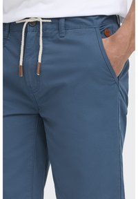 Pantalones cortos azules con una textura suave, que cuentan con una cintura con cordón y un parche de logo de cuero marrón. Se pueden ver bolsillos laterales.