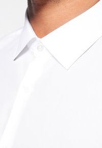 Witte katoenen overhemd met een puntige kraag, een sluiting met één knoop en een gladde textuur. Close-up van de kraag en stof.