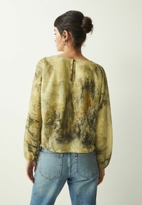 Langärmlige Bluse aus olivgrünem Stoff, mit einem Naturdruck von Bäumen in gedämpften Farben und einem Schlitzdetail am hinteren Ausschnitt.