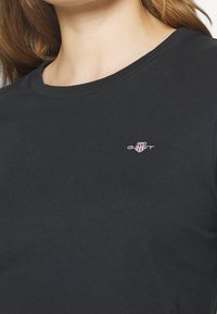 Czarny bawełniany t-shirt z okrągłym dekoltem i krótkimi rękawami. Posiada małe haftowane logo na piersi. Klasyczny krój i gładka tekstura.