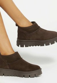 Bottes chelsea en daim marron avec un bout rond, des détails en bande élastique et des semelles en caoutchouc épaisses. Présente une texture lisse et des coutures contrastantes.
