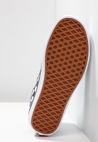 Černobílá skate obuv s gumovou podrážkou s hexagonálním vzorem a bílým okrajem. Boční profil ukazuje charakteristický design a texturu pro lepší přilnavost.