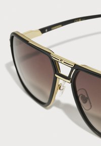 Ochelari de soare negri cu un cadru din metal auriu, lentile întunecate cu un gradient și pernuțe de nas transparente. Prezentând un design în două tonuri și o formă elegantă, unghiulară.