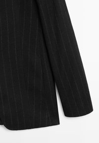 Czarna marynarka w pionowe prążki, wykonana z teksturowanej tkaniny. Posiada gładki kołnierz oraz wygięty brzeg rękawa.