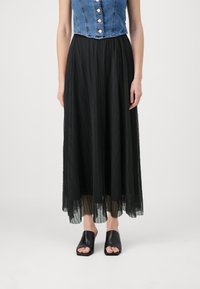 Denim crop topp med metallknapper, kombinert med en flytende svart plissert skjørt og åpne svarte lær sko.
