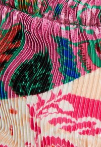 Närbild av veckat tyg med livfullt blommönster i rosa, grönt, blått och rött som visar texturerade veck och färgkontraster.