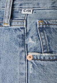 Jasnoniebieskie dżinsy z wykończeniem w stylu vintage, widocznym szwem, mosiężnym guzikiem oraz metką z napisem "C of H."