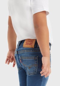 Vaqueros de mezclilla azul con un parche de cuero de Levi's en la parte posterior de la cintura. El diseño presenta clásicos bolsillos traseros y costuras amarillas.