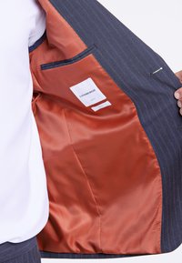 Marineblå randig kostymjacka med en insida av klar orange satin, som har en ficka och klädesetikettens detaljer.