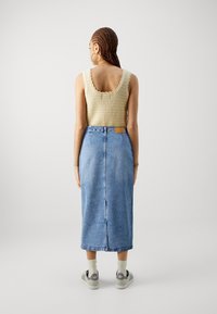 Pletený top bez rukávů v béžové barvě s vlnitými okraji, spárovaný s modrou džínovou sukní po kolena, která má rozparek vzadu a kožený štítek v pase.