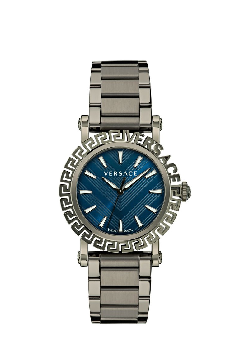 Montre à cadran bleu avec un bracelet en métal de couleur argentée. Présente une lunette à motif clé grec, des index argentés et une étiquette de fabrication suisse.