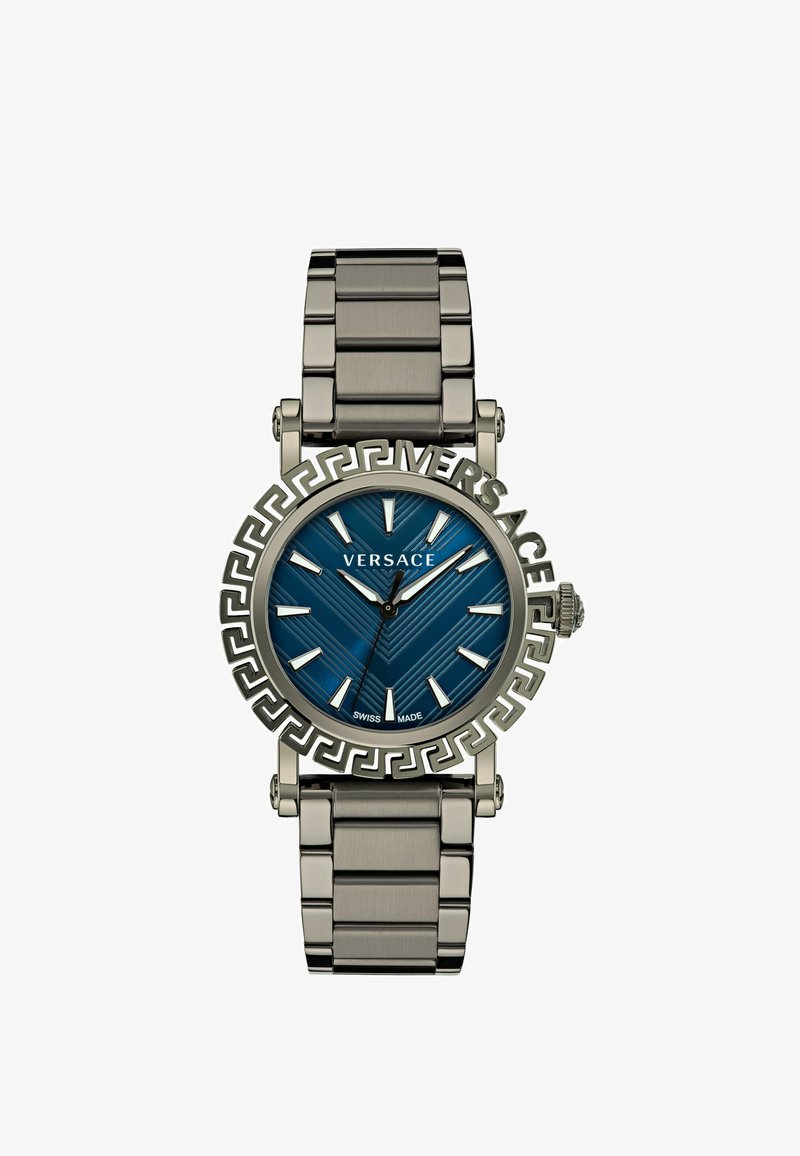 Montre à cadran bleu avec un bracelet en métal de couleur argentée. Présente une lunette à motif clé grec, des index argentés et une étiquette de fabrication suisse.