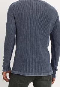 Pull bleu marine à manches longues avec un effet côtelé texturé, un col rond et un ourlet avec un bord contrastant subtil. Coupe décontractée, sans éléments visibles en métal.