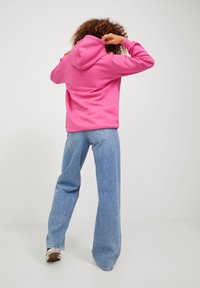 Vaaleanpunainen huppari, jossa on huppu, resorit hihansuissa ja rento istuvuus. Yhdistetty vaaleansinisiin leveälahkeisiin farkkuihin ja lenkkareihin. Yksivärinen tausta.