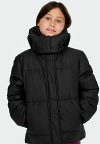 Crna podstavljena jakna s visokim ovratnikom, vidljivim šavovima i opuštenim krojem. Materijal je glatke teksture s mat završetkom.