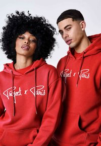 Sudaderas rojas con la inscripción blanca "Project x Paris," con cordones y bolsillos frontales, exhibidas en dos modelos. Textura de tela suave.
