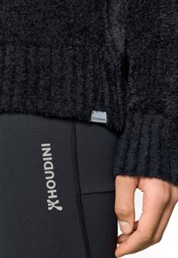 Melnā faktūras džemperis ar ribotiem manžetēm, kombinēts ar melnām legingām ar baltu "Houdini" zīmolu sānos. Mīksts, pūkains materiāls.