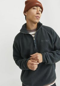 Fleece pullover i mørkegrå med halv-zipped design, broderet logo og ribbede manchetter. En hyggelig, tekstureret finish skabt til varme.
