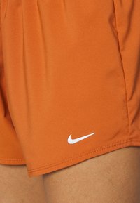 Oranssit urheilushortsit, jotka on valmistettu sileästä kankaasta. Shortsien vasemmassa alakulmassa on valkoinen Nike-logo ja siistit reunat.