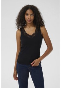Haut sans manches noir avec un col en V, comportant des finitions en dentelle le long du décolleté et un ourlet légèrement effiloché. Associé à un jean bleu.