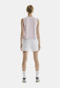 Lichtroze mouwloos topje, gecombineerd met witte shorts. Model draagt grijze sneakers met gele accenten en witte sokken. Gladde stoftextuur.