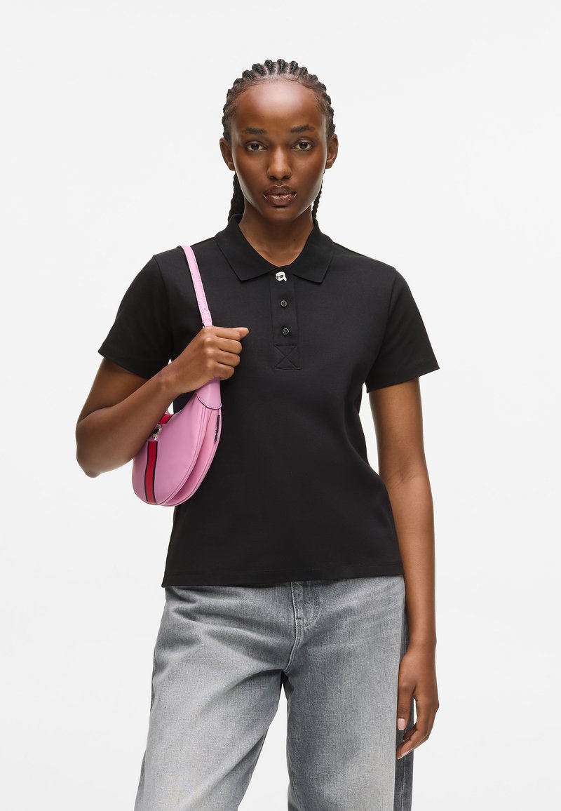 Čierne polokošeľa s golierom, zapínaním na tri gombíky a krátkymi rukávmi, v kombinácii s ružovou crossbody kabelkou. Svetlo pranie denimové džínsy.