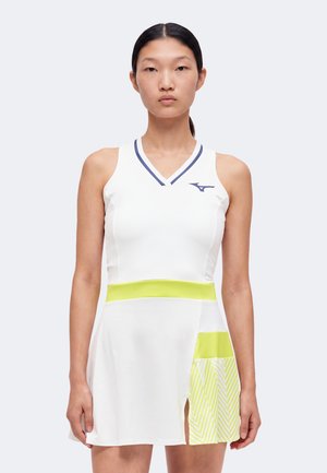 Frau trägt weißes ärmelloses Tenniskleid mit marineblauer Umrandung, limonengrünem Taillenbund und gemusterter limonengrüner Kellerfalte an der Rockseite.
