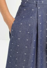 Jeanskjol i mörkblått med vita broderade lövmönster. Har bälte, fickor och texturerad tyg. Skräddarsydd passform med plisseringar.