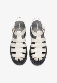 White platform sandals with a crisscross strap design, adjustable buckle, and a textured black sole. Smooth finish, open-toe style.