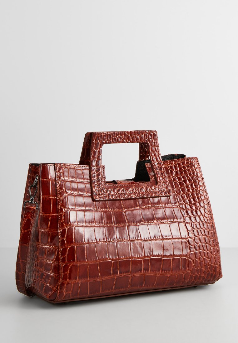 Sac à main bordeaux brillant avec un motif en crocodile, une anse découpée carrée, un grand compartiment principal et une bandoulière amovible.