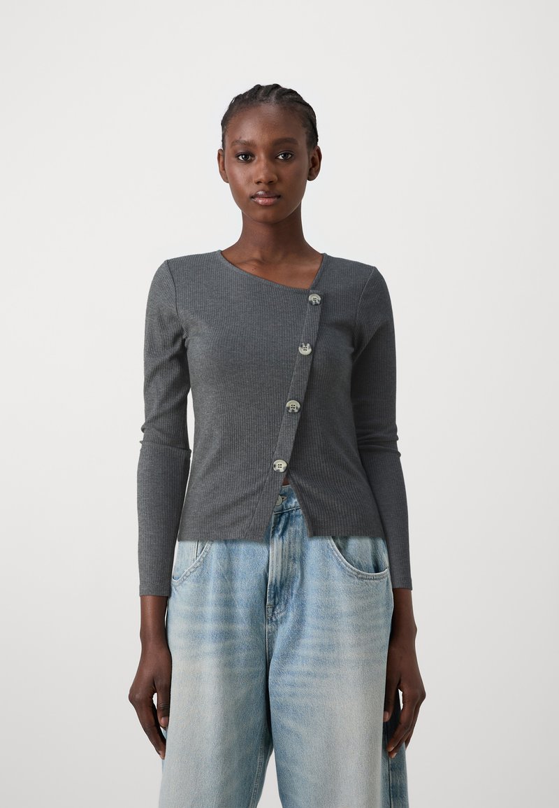 Cardigan long à manches longues gris côtelé avec un décolleté en V et cinq boutons ronds à l'avant, porté sur un jean large bleu clair.