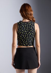 Svart crop top med gult blomsterdesign, med blonderkant ved halsen, kombinert med et tettsittende svart miniskjørt. Glatt, lett stoff.