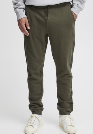 Olive green jogger pants made of soft fabric with an elastic waistband, featuring a drawstring and side pockets. Worn with white sneakers.