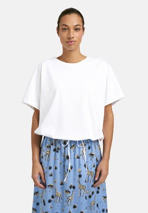 Woman wearing plain white oversized t-shirt tucked into blue drawstring pants with giraffe and plant prints, standing against a light background.