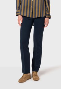 Mörkblå byxor med slim fit, tillverkade av ett strukturerat tyg. Kombinerat med ljusbruna sneakers och en randig skjorta med knappar.