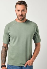 Bavlněné tričko s kulatým výstřihem v tlumené zelené barvě, krátké rukávy, žebrovaný límec, slim fit, hladká textura s viditelnými švy.