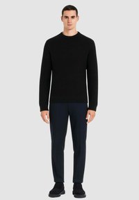 Maglione nero a maglia con scollo rotondo, polsini e orlo a costine, abbinato a pantaloni sartoriali blu navy e scarpe nere. Design semplice, texture senza cuciture.