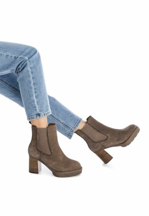 Botas de ante marrón hasta el tobillo con paneles elásticos en los laterales, un tacón grueso y suelas de goma texturizadas, combinadas con unos vaqueros cortos azules.