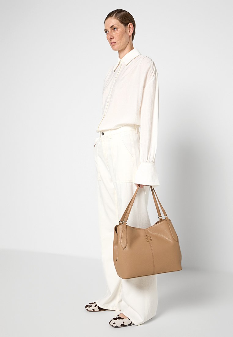 Braune Lederhandtasche mit doppelten Trageriemen, weicher Struktur, strukturiertem Finish und genähten Akzenten, kombiniert mit einem weißen, lockeren Outfit.