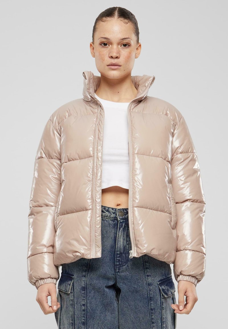Polstret jakke i lys beige med glanset finish, høy krage, glidelås og elastiske mansjetter. Brukt over en hvit crop-top.