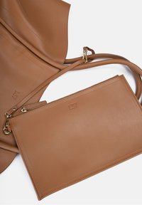 Tan leren handtas met een gladde textuur, voorzien van een afneembare ritstas en fijne stiksels. Accenten in goudkleurige hardware.