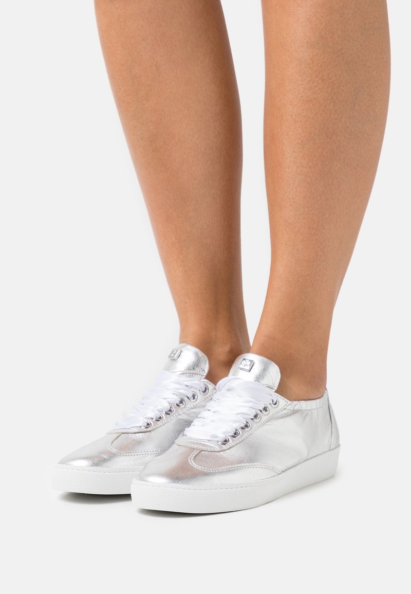 Silver metallic sneakers med slät läderstruktur, vita snören, rund tå och låg gummisula. Ögla och logotyp på tungan.