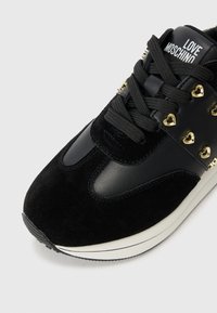 Zwarte sneaker van suède en leer, met hartvormige gouden studs, zwarte veters en een witte zool. Merken op de tong.