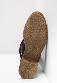 Zapato negro con una suela de goma texturizada, que presenta un patrón visiblemente desgastado y una parte superior lisa sin hardware o acentos prominentes.