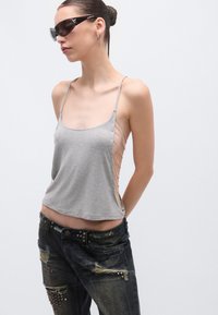 Hall hallatud lühike tanktop külgpandlatega, kombineeritud kulunud tumedate teksadega, millel on naelutatud detailid ja narmendav ääris.